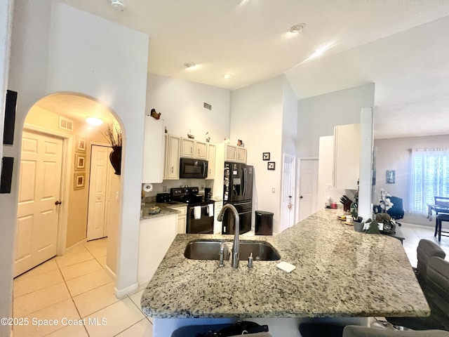 kitchen featuring visible vents, arched walkways, a peninsula, black appliances, and a sink