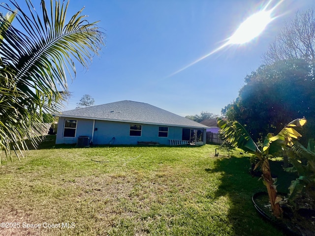 rear view of house with a yard, stucco siding, cooling unit, and fence