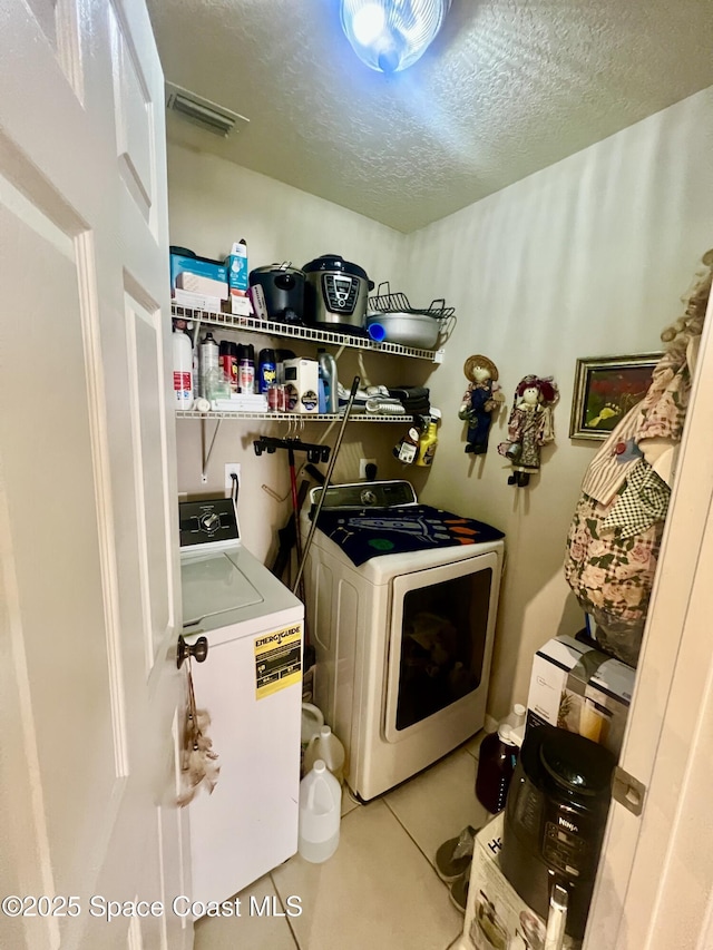 laundry area featuring a textured ceiling, light tile patterned floors, laundry area, visible vents, and washer and clothes dryer