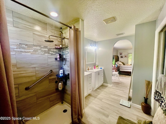 ensuite bathroom with visible vents, wood finished floors, tiled shower, and vanity