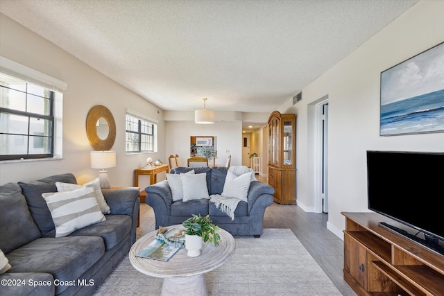 living room with visible vents, a textured ceiling, baseboards, and wood finished floors