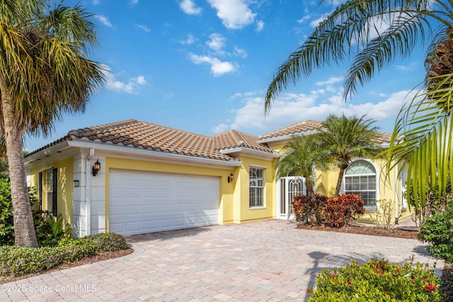 mediterranean / spanish house with a garage, a tile roof, decorative driveway, and stucco siding