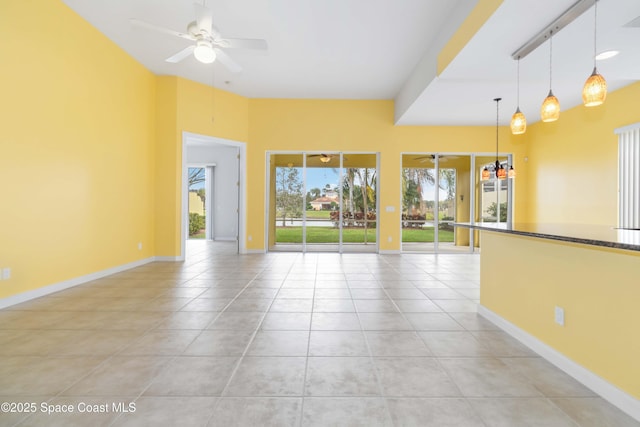 empty room with light tile patterned flooring, plenty of natural light, a ceiling fan, and baseboards