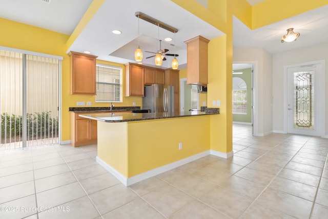 kitchen featuring light tile patterned floors, dark stone counters, decorative light fixtures, a peninsula, and freestanding refrigerator