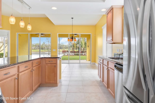 kitchen with light tile patterned floors, dark stone counters, appliances with stainless steel finishes, hanging light fixtures, and a sink