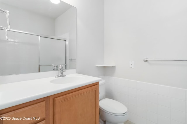 bathroom with toilet, vanity, tile walls, wainscoting, and an enclosed shower