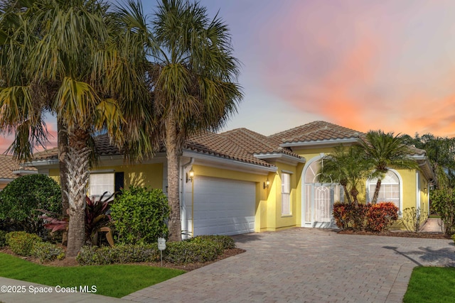 view of front of home featuring a garage, a tile roof, decorative driveway, and stucco siding