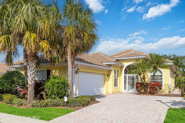 view of front facade featuring a garage, a tiled roof, decorative driveway, and stucco siding