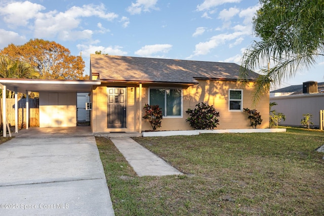 view of front of house featuring concrete block siding, a front yard, fence, concrete driveway, and a carport