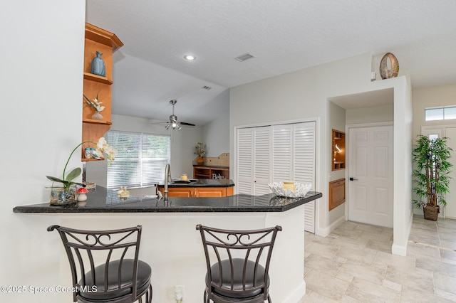 kitchen featuring lofted ceiling, a peninsula, a breakfast bar, and visible vents