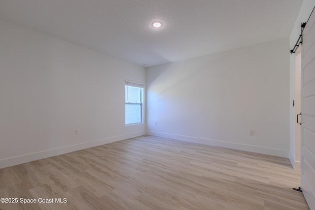 spare room with light wood-type flooring, a barn door, and baseboards