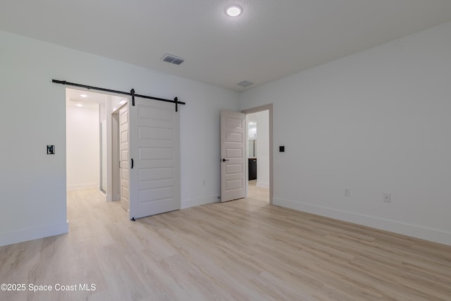 spare room featuring light wood-style floors, a barn door, visible vents, and baseboards