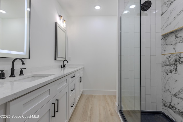 full bathroom with wood finished floors, double vanity, a sink, and a walk in shower