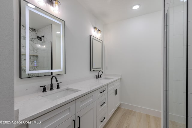 bathroom featuring tiled shower, a sink, baseboards, and double vanity