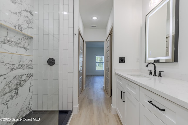 full bath featuring tiled shower, vanity, baseboards, and wood finished floors