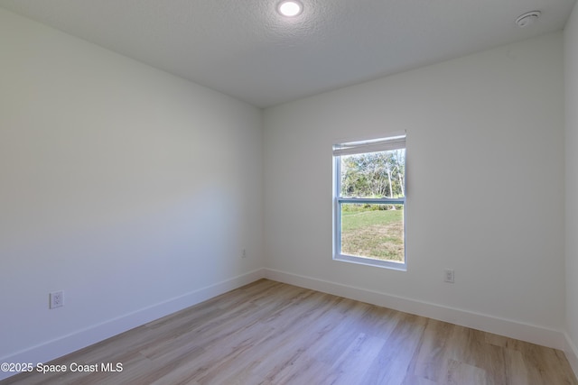 spare room with light wood finished floors, baseboards, and a textured ceiling