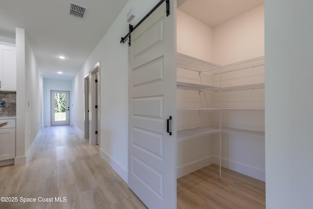 hall with a barn door, visible vents, baseboards, light wood-style flooring, and recessed lighting