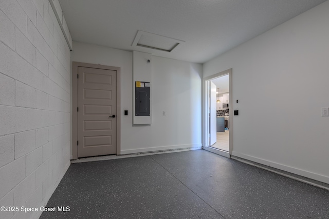 spare room featuring attic access, concrete block wall, electric panel, and speckled floor