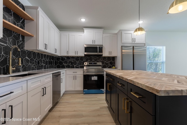 kitchen featuring white cabinets, butcher block countertops, stainless steel appliances, dark cabinetry, and a sink