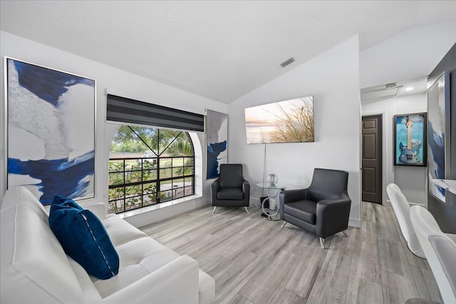 living area featuring vaulted ceiling, wood finished floors, and visible vents