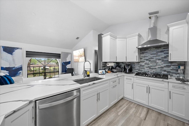 kitchen with black gas cooktop, stainless steel dishwasher, vaulted ceiling, a sink, and wall chimney exhaust hood