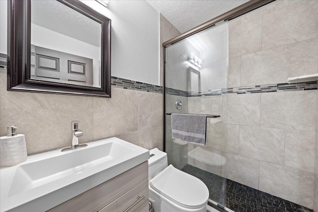 bathroom featuring toilet, a tile shower, a textured ceiling, vanity, and tile walls