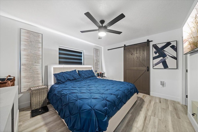 bedroom with a textured ceiling, a barn door, wood finished floors, a ceiling fan, and baseboards