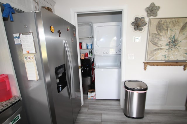 kitchen with baseboards, stainless steel refrigerator with ice dispenser, and stacked washer / drying machine