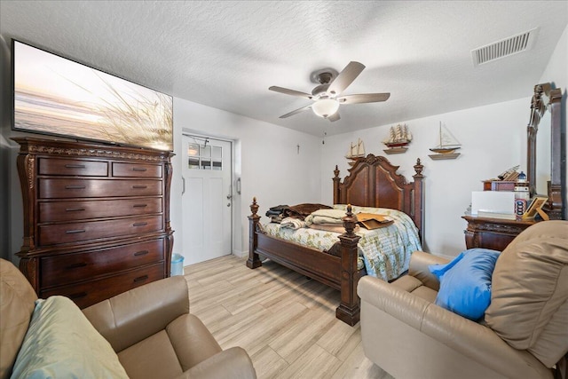 bedroom with a textured ceiling, a ceiling fan, visible vents, and light wood-style floors