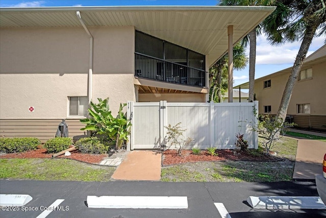 back of property featuring uncovered parking, a gate, fence, and stucco siding