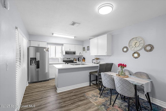 kitchen with visible vents, white cabinets, dark wood finished floors, appliances with stainless steel finishes, and a peninsula