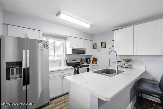 kitchen with stainless steel appliances, a peninsula, a sink, white cabinetry, and a kitchen breakfast bar