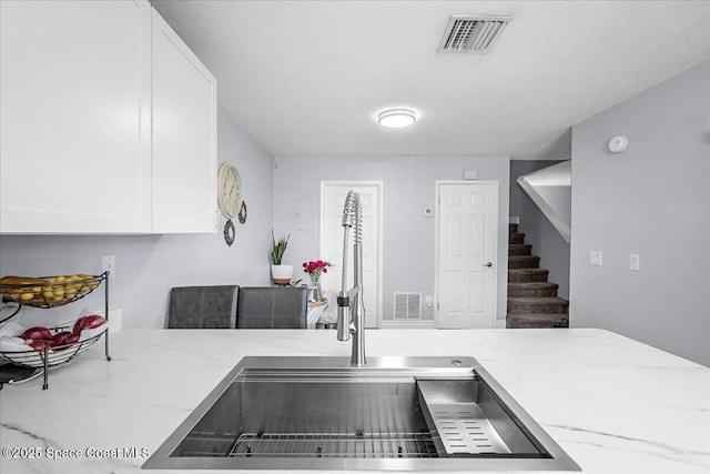 kitchen featuring white cabinetry, visible vents, light stone counters, and a sink