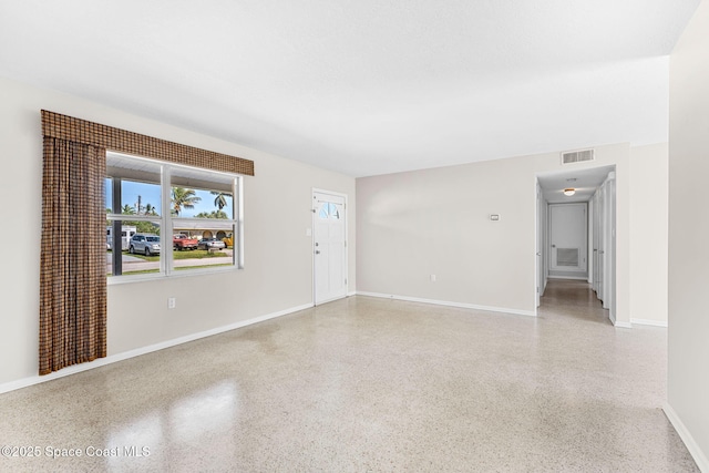 empty room featuring baseboards, visible vents, and light speckled floor