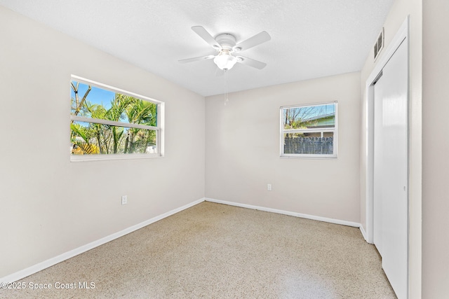 unfurnished bedroom featuring multiple windows, a textured ceiling, baseboards, and speckled floor