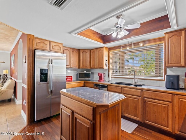 kitchen featuring crown molding, a tray ceiling, decorative backsplash, appliances with stainless steel finishes, and a sink