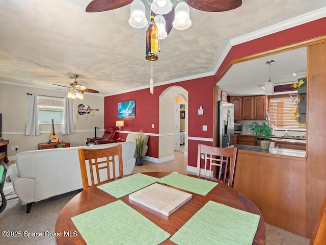 dining area with crown molding, light tile patterned floors, arched walkways, and ceiling fan