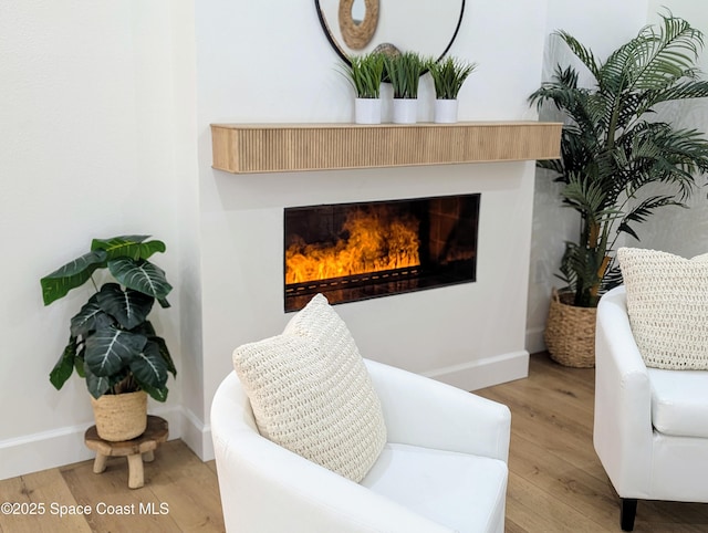 sitting room with baseboards, a lit fireplace, and wood finished floors