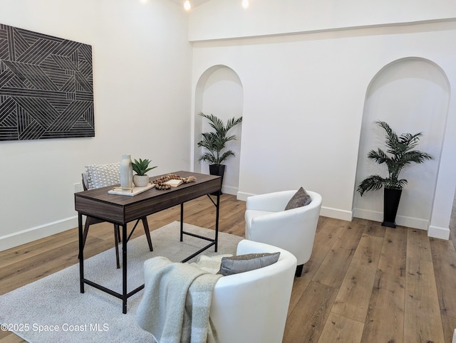 office featuring light wood finished floors, arched walkways, and baseboards