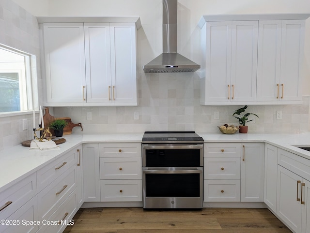 kitchen with range with two ovens, decorative backsplash, white cabinets, light wood-style floors, and wall chimney range hood