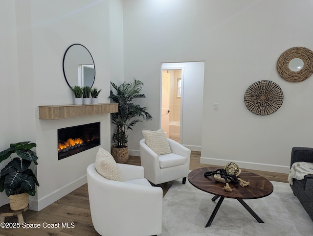 living area featuring wood finished floors, baseboards, and a warm lit fireplace