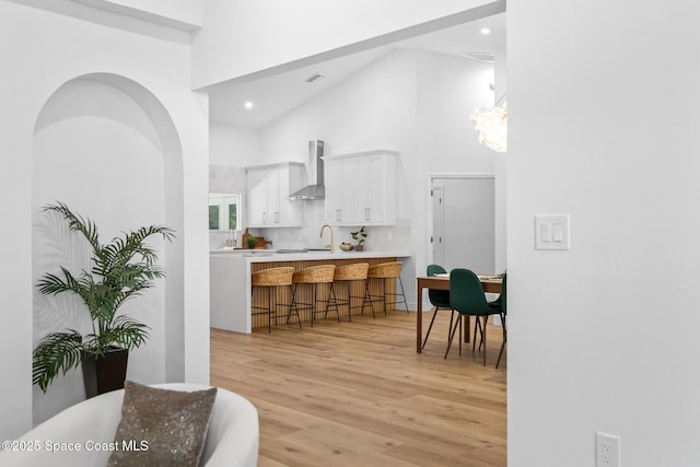kitchen with a breakfast bar, a high ceiling, light wood-style flooring, a sink, and wall chimney exhaust hood