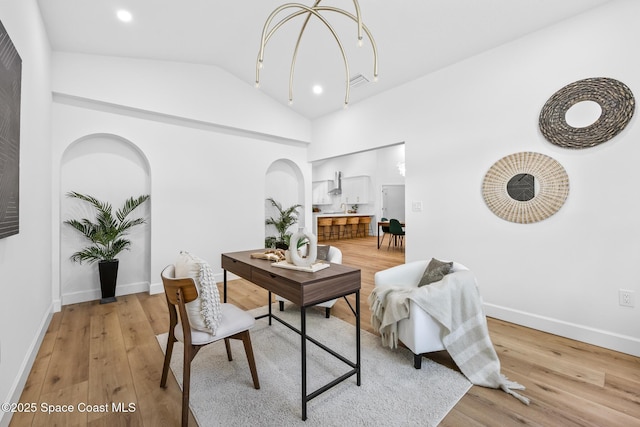 office space featuring baseboards, visible vents, lofted ceiling, light wood-style flooring, and arched walkways