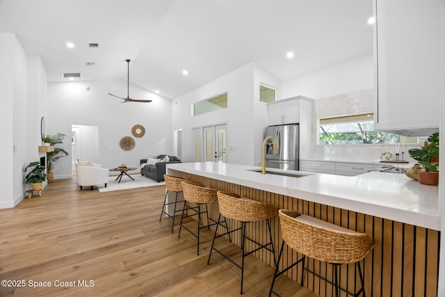 kitchen featuring open floor plan, high vaulted ceiling, light wood-type flooring, stainless steel refrigerator with ice dispenser, and white cabinetry