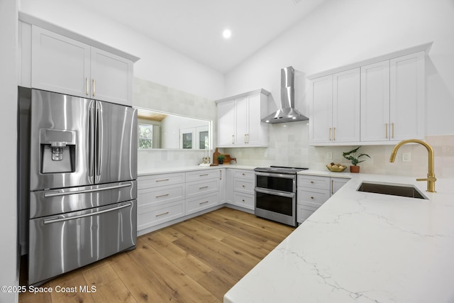 kitchen featuring light stone countertops, light wood finished floors, a sink, appliances with stainless steel finishes, and wall chimney exhaust hood