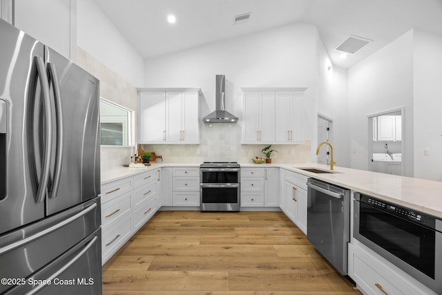 kitchen featuring visible vents, a sink, stainless steel appliances, wall chimney exhaust hood, and separate washer and dryer