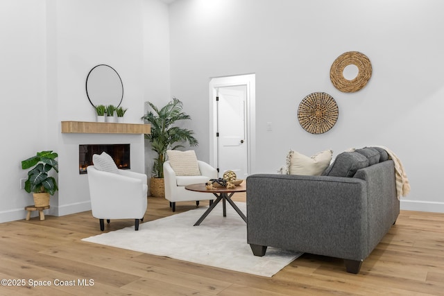 living area with light wood finished floors, a glass covered fireplace, a high ceiling, and baseboards