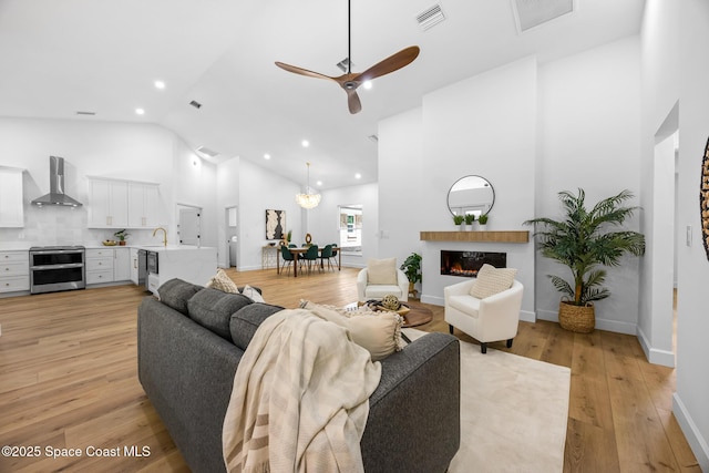living area featuring a lit fireplace, visible vents, a ceiling fan, and light wood-style floors