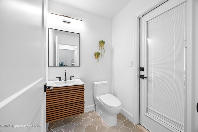 half bath with tile patterned floors, baseboards, toilet, and vanity