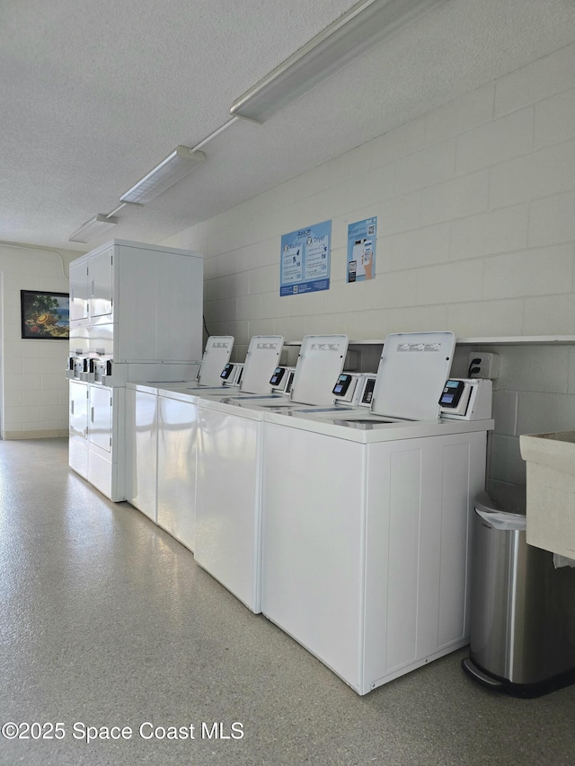 community laundry room with a textured ceiling, separate washer and dryer, stacked washing maching and dryer, and concrete block wall